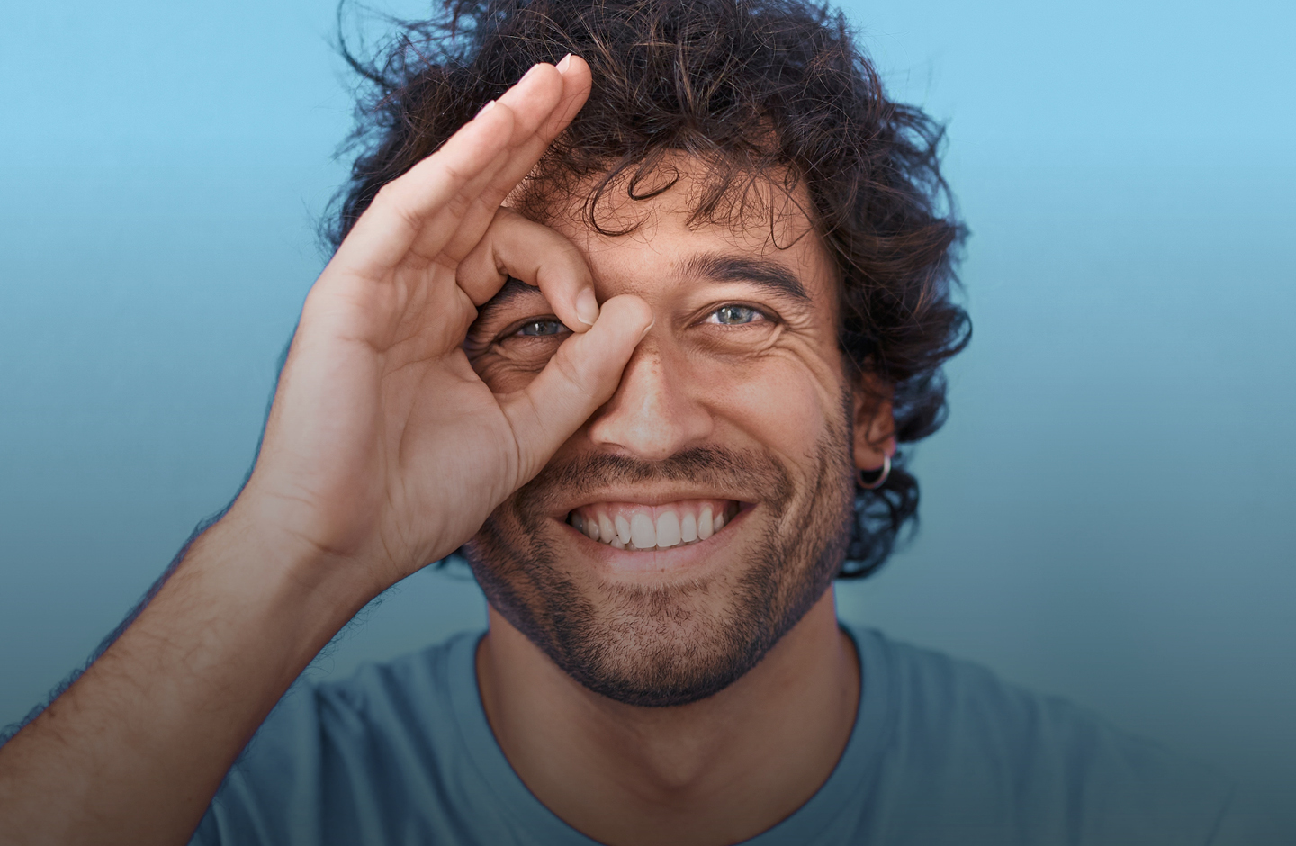 Ein Mann formt mit seinen Fingern einen Kreis und hält ihn lachend vor sein Auge.